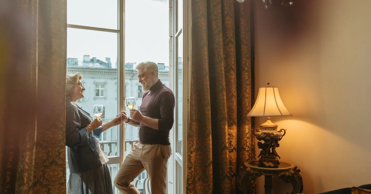 Encantadora pareja mayor compartiendo un momento con vino junto a la ventana, evocando calidez y elegancia.