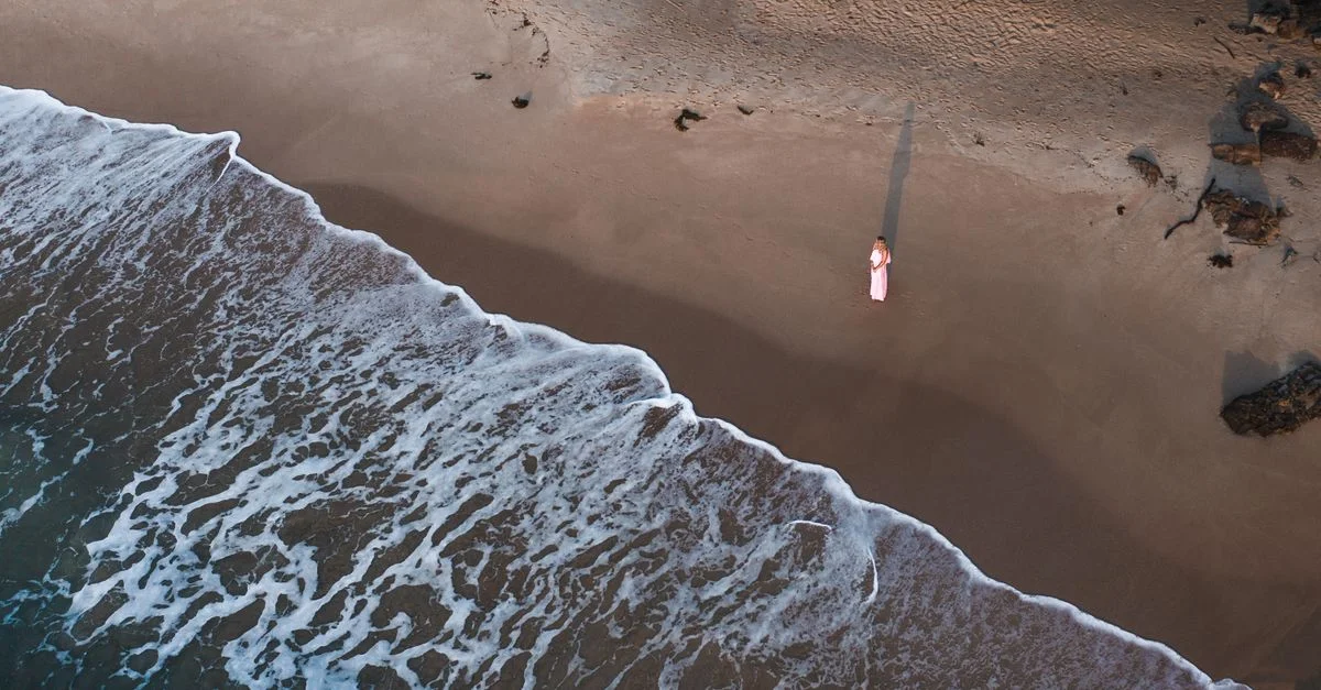 Toma de dron de una mujer de pie en la Playa Narrawallee, NSW, Australia.