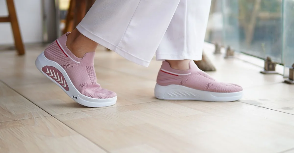 Primer plano de zapatillas deportivas rosas de punto sin cordones combinadas con pantalones blancos, ideales para un look casual.