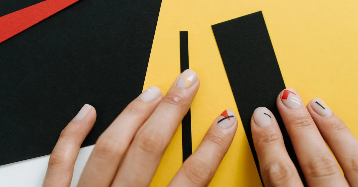 Primer plano de arte de uñas moderna con formas geométricas en una collage de papel amarillo y negro.