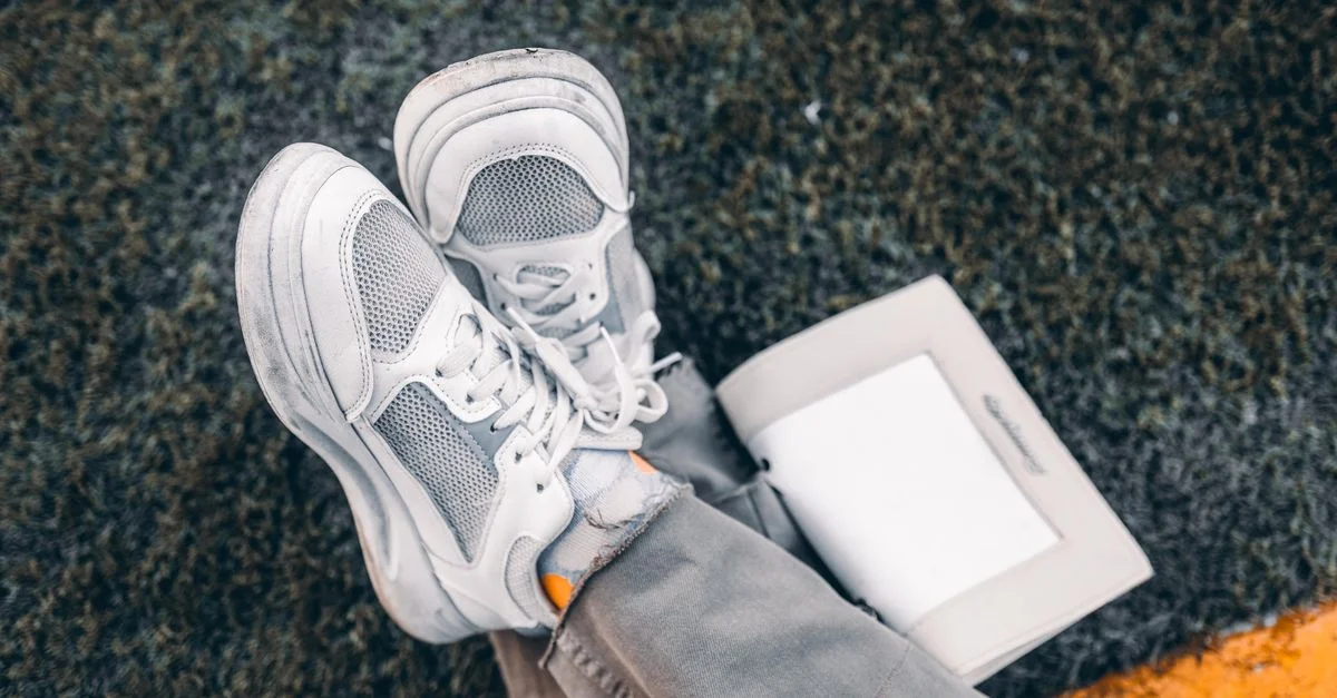 Zapatillas blancas casualmente colocadas sobre hierba con un libro abierto, transmitiendo una vibra relajada al aire libre.