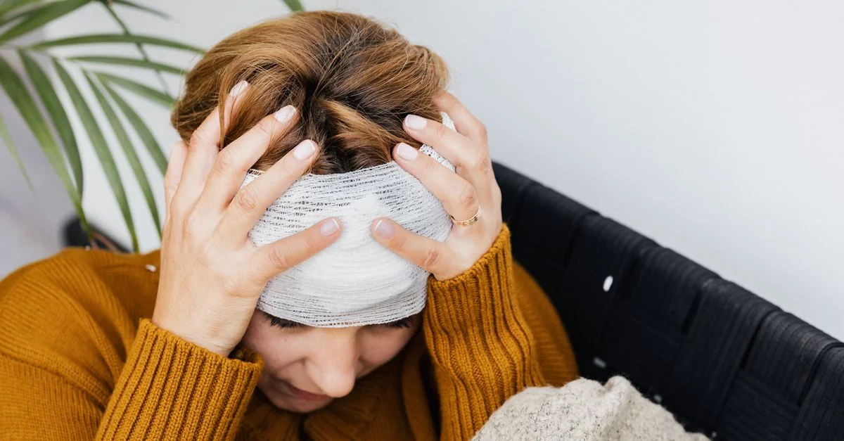 Mujer con lesión en la cabeza sosteniendo su cabeza con dolor en interiores.