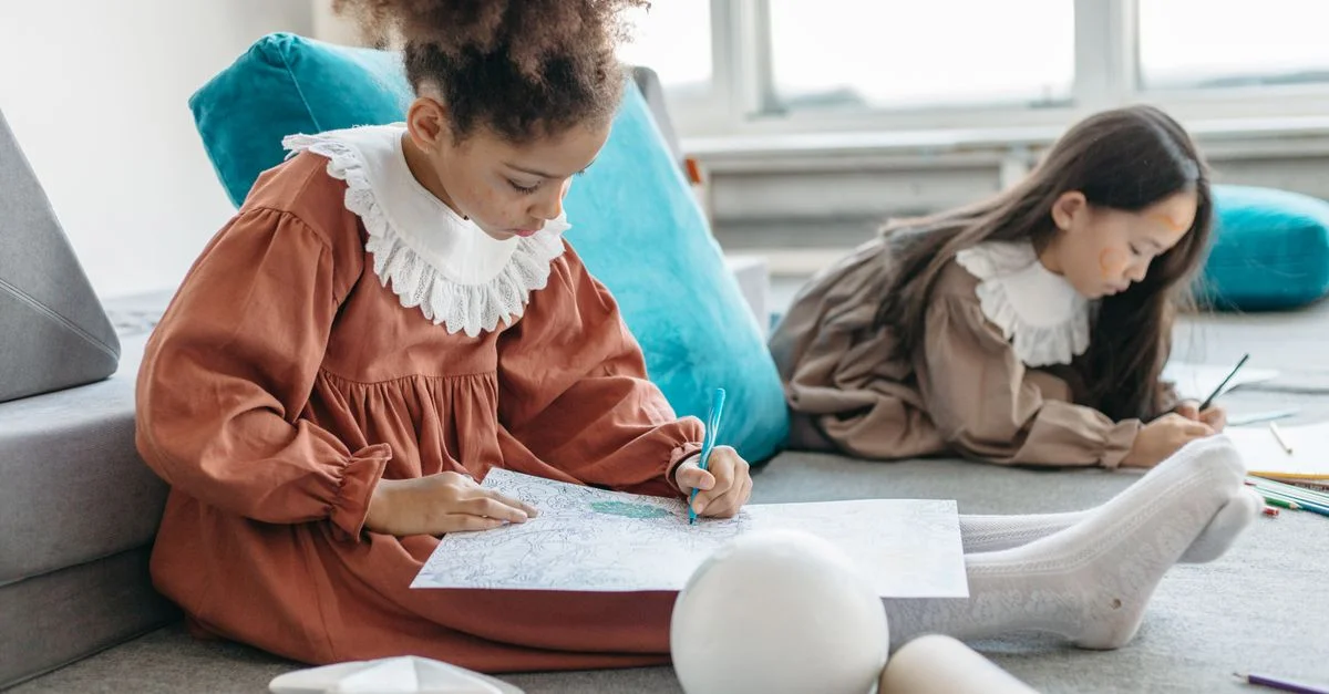 Dos niñas disfrutan dibujando y coloreando en interiores, mostrando creatividad y concentración.