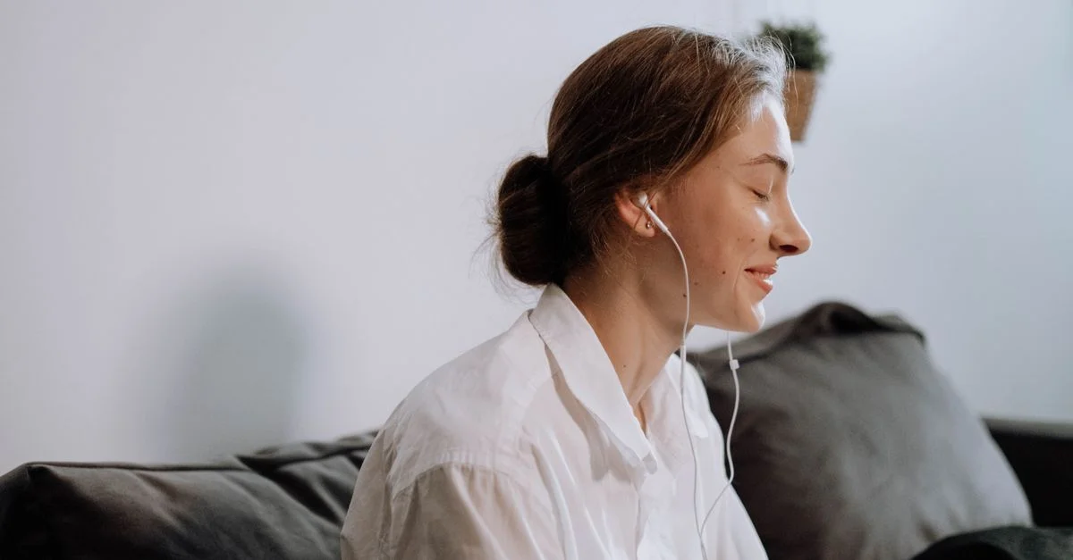 Vista de perfil de una mujer sonriendo con auriculares, relajándose en interiores.