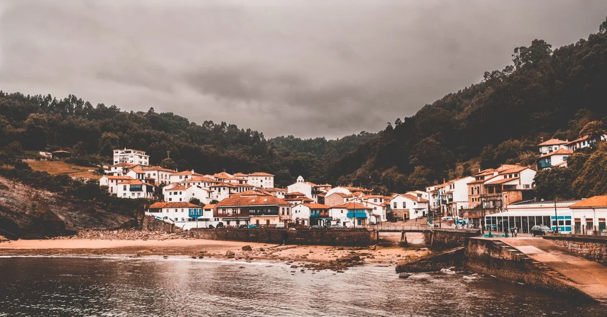Encantador pueblo costero de Candás, España, bajo cielos nublados con casas tradicionales a lo largo de la costa.