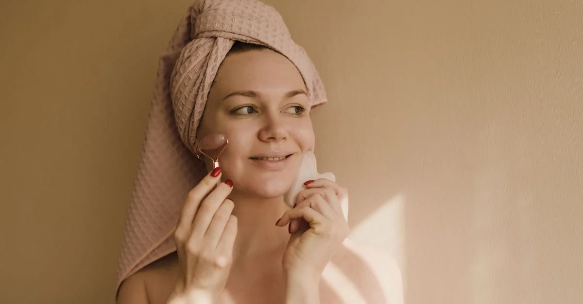 Mujer sonriente utilizando un rodillo facial y gua sha en una relajante rutina de cuidado de la piel.