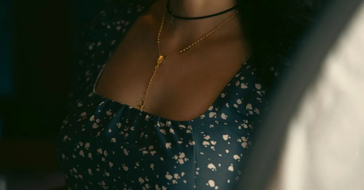 Primer plano del escote de una mujer adornado con un collar de oro y una blusa floral, capturando elegancia y sutileza.
