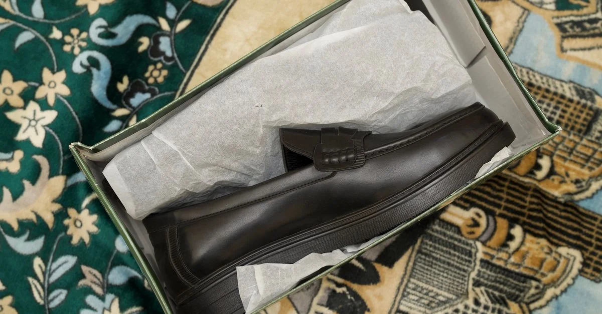 Mocasines de cuero negro presentados elegantemente en una caja, mostrando un diseño moderno y minimalista.