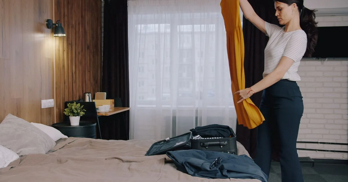 Una mujer dobla la ropa mientras hace la maleta en una acogedora habitación de hotel con una decoración moderna.