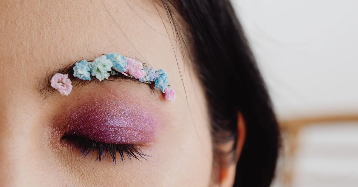 Primer plano de un diseño floral creativo de cejas con sombra de ojos brillante en un ojo cerrado.