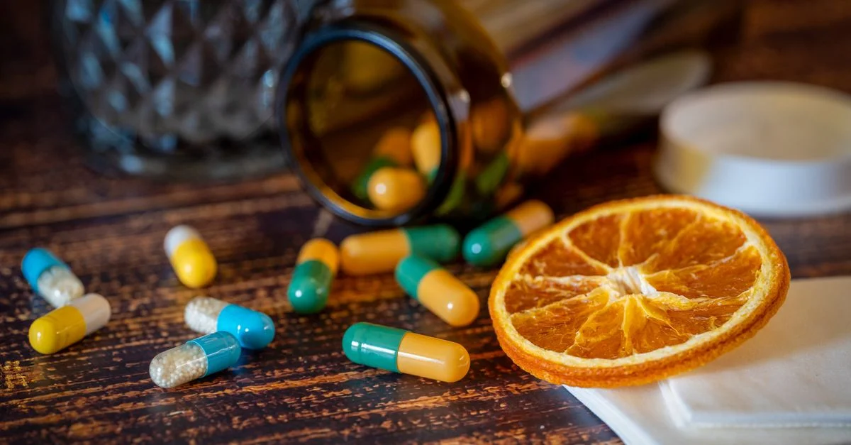 Acercamiento de vitaminas, pastillas y una rodaja de naranja seca para aliviar el resfriado.