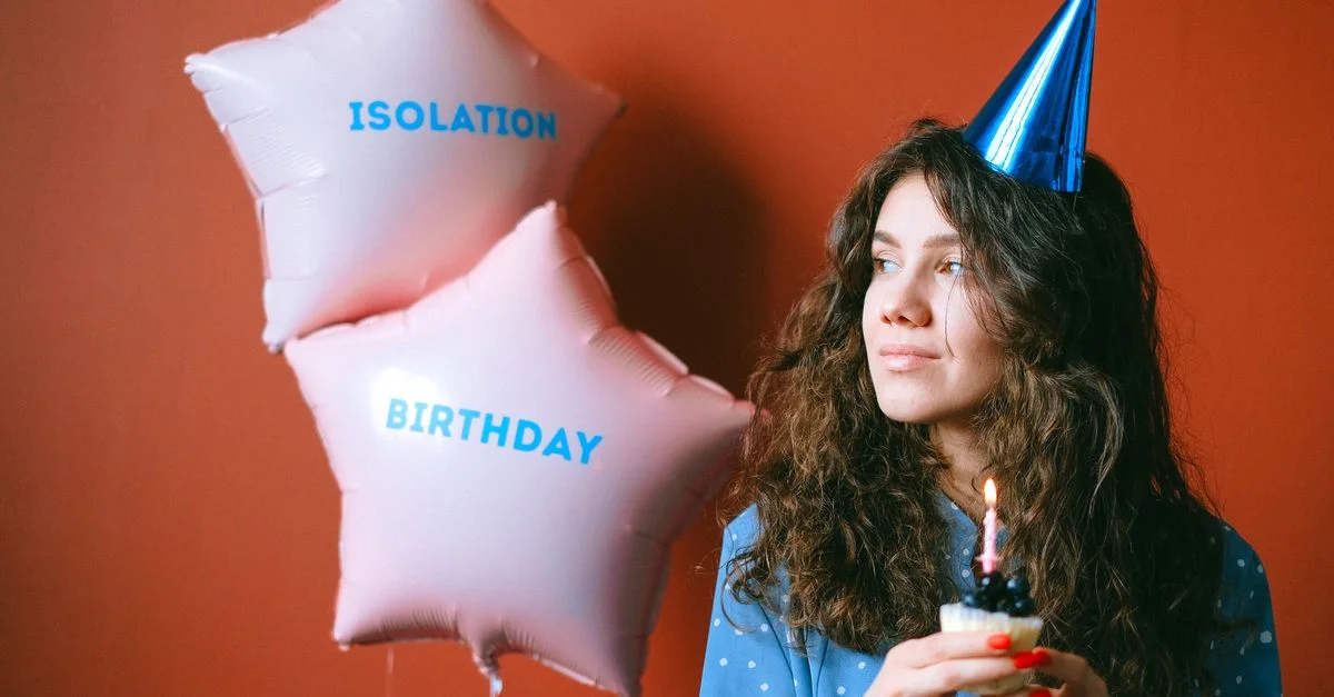 Mujer joven con gorro de cumpleaños y cupcakes durante una celebración aislada con globos.