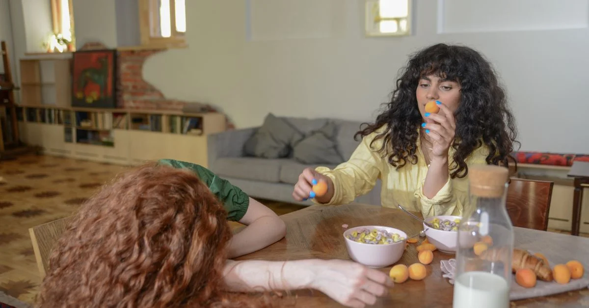 Dos mujeres cenando con albaricoques, cereales y leche en un ambiente acogedor.