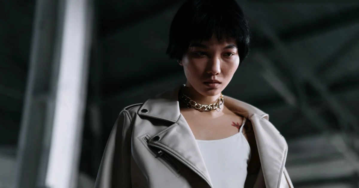 Una mujer a la moda con expresión seria, vistiendo una chaqueta de cuero y collar de cadena.