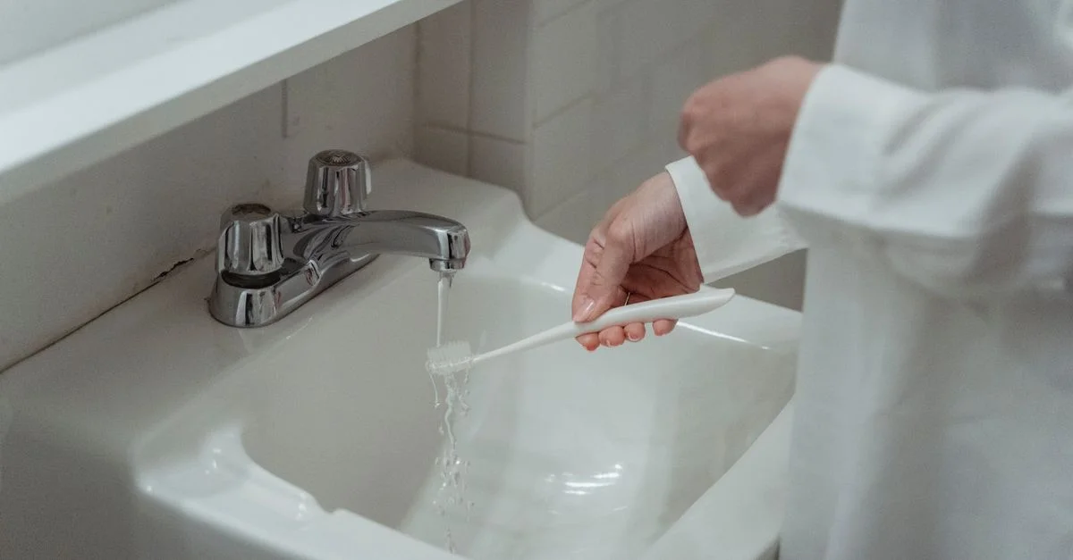 Primer plano de una mujer lavando un cepillo de dientes bajo el grifo del lavabo del baño, centrándose en la higiene dental