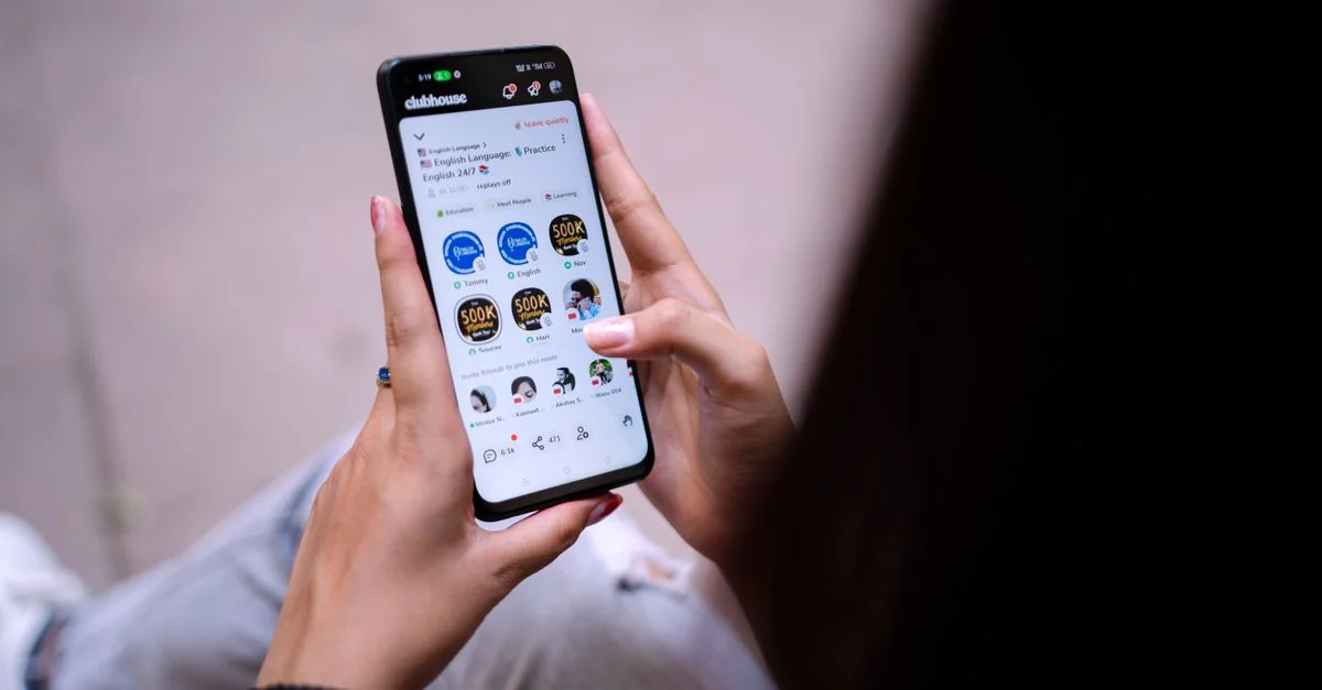 Primer plano de una mujer usando un smartphone con una aplicación de redes sociales abierta. Manos sosteniendo el dispositivo.