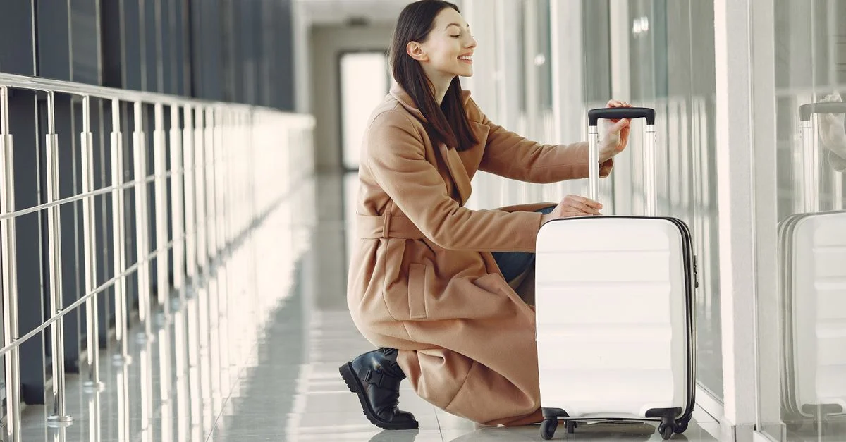Mujer sonriente con maleta sentada en un pasillo moderno de aeropuerto.