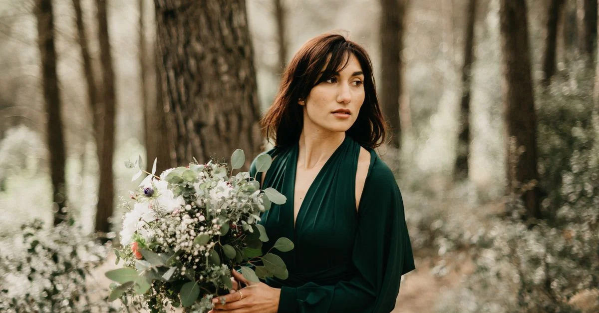 Retrato de una mujer con un vestido verde sosteniendo un ramo en un bosque sereno